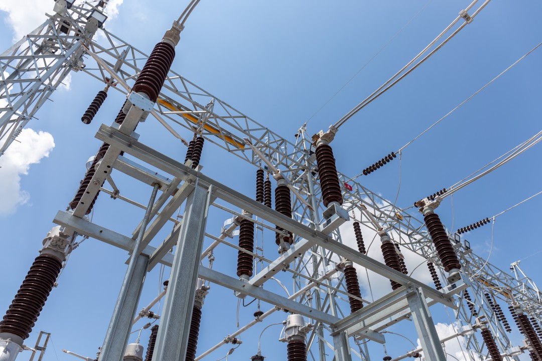 High-voltage substation lattice structures with porcelain insulators against blue sky.