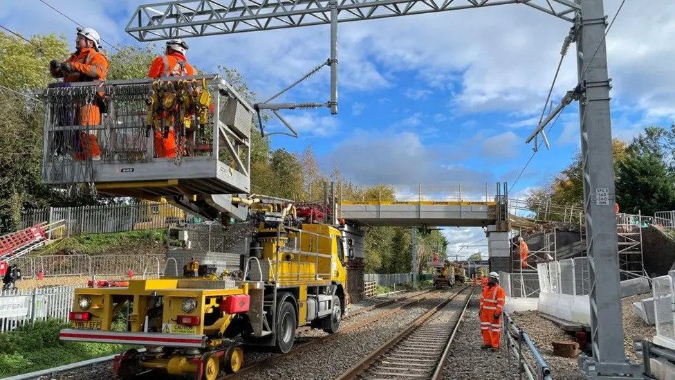 Engineers on an elevated platform installing overhead line equipment on a railway bridge.